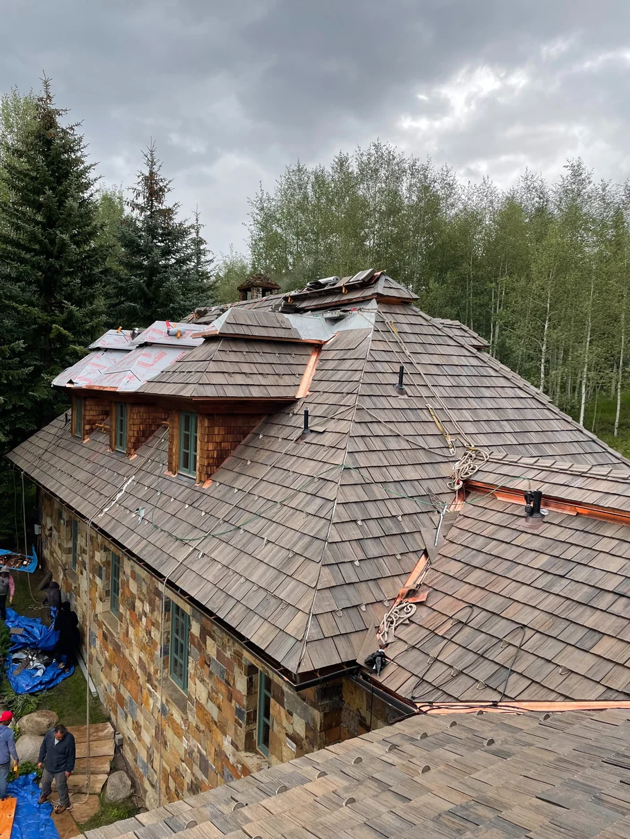 Eagle Park Drive Aspen stone home with Brava synthetic shake roof, copper valley flashing, and dormers during installation