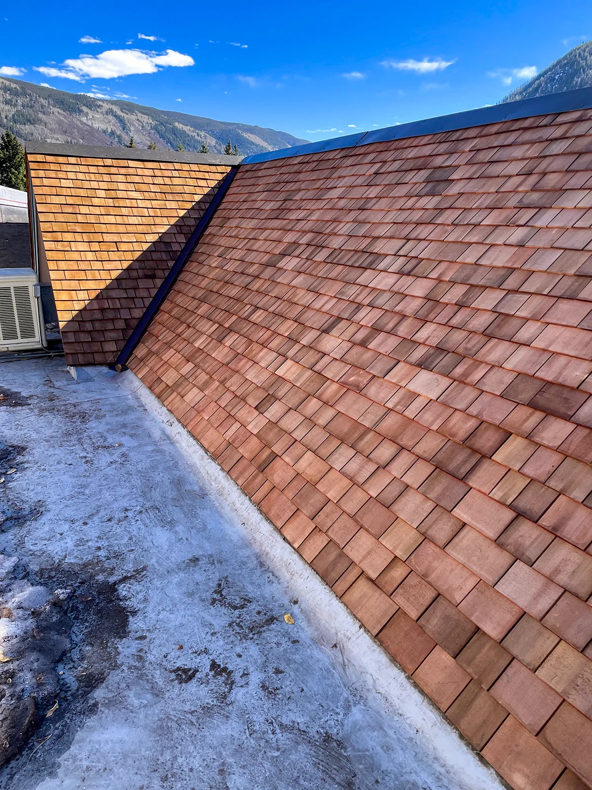 New reddish wood shingles with dark metal valley flashing on a steep roof