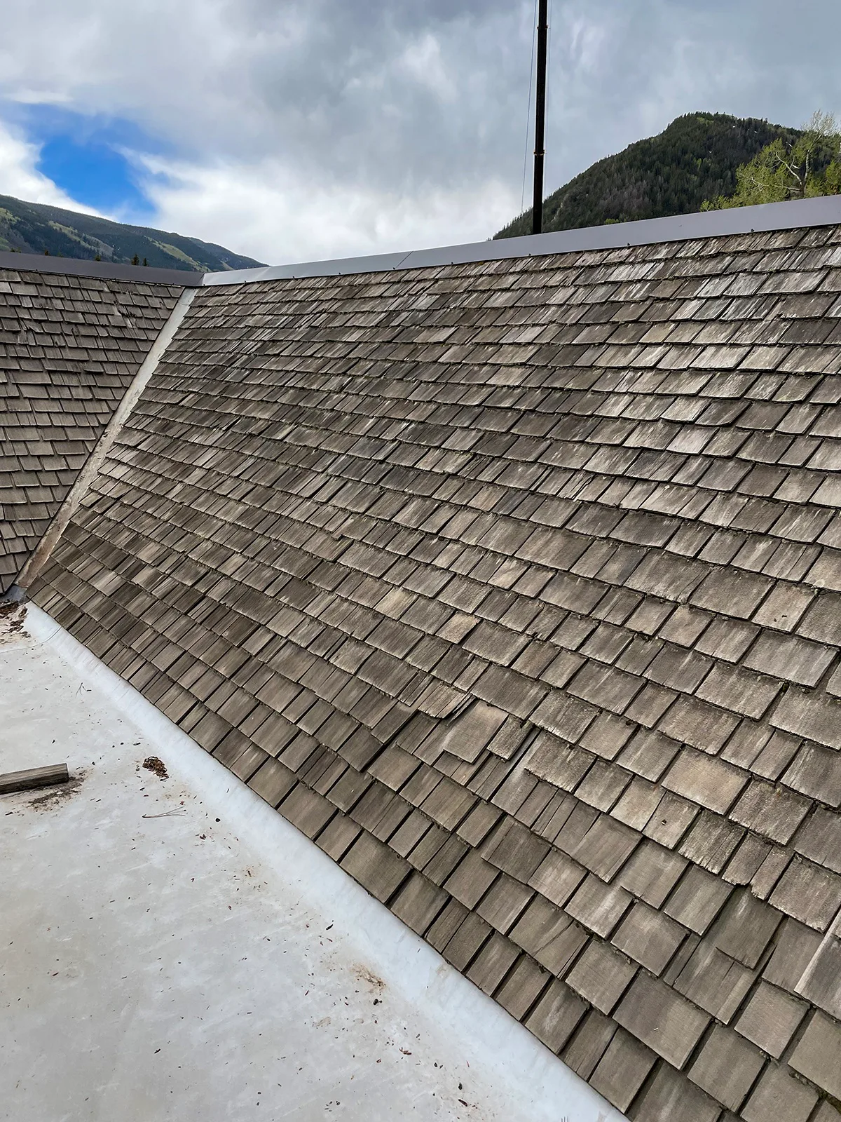 Weathered wood shingles with split, cupped, and thinning edges on a steep roof
