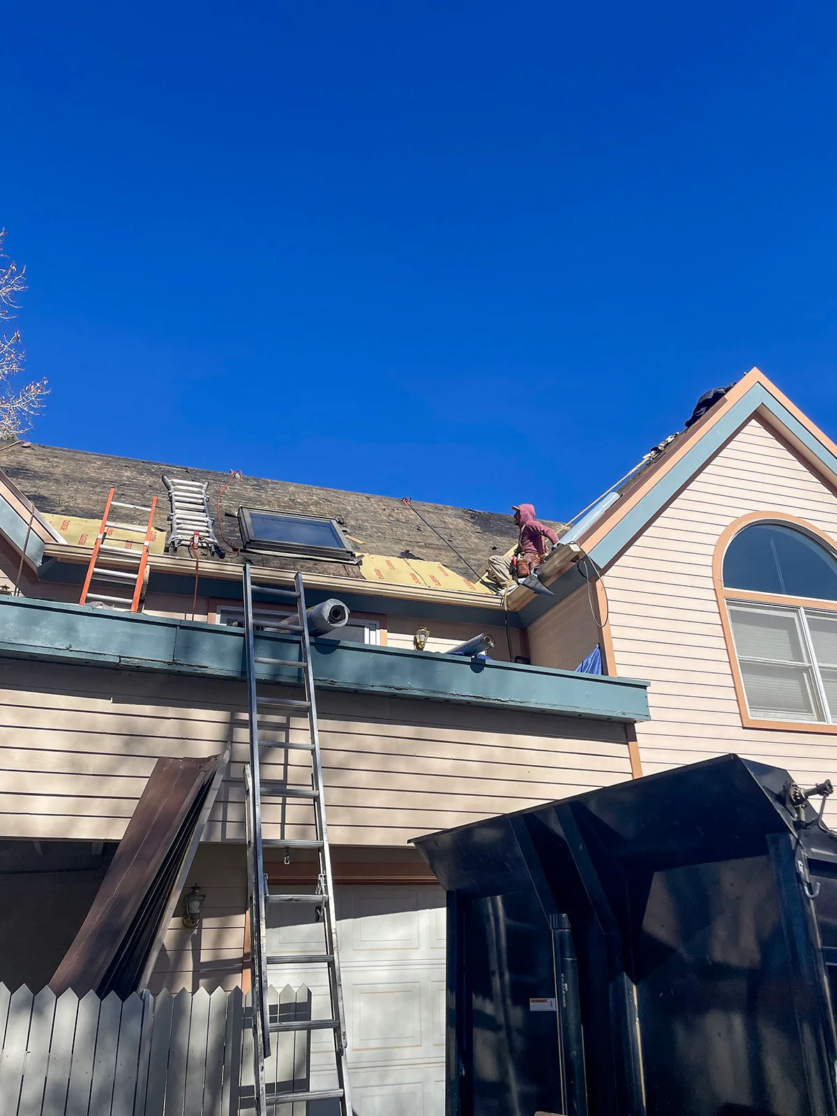Roofer working beside a skylight on a stripped roof during a wood-shingle replacement