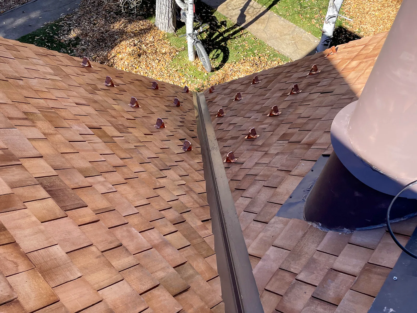 Metal valley and rows of snow guards installed between new wood-shingle roof planes