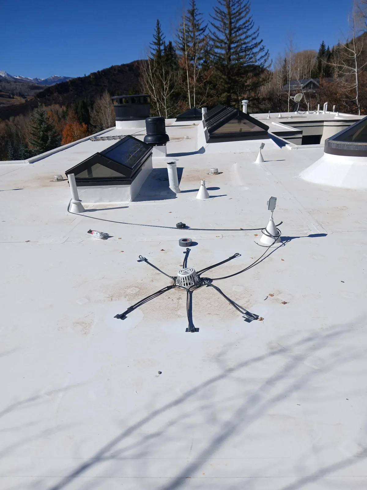 Finished white membrane roof around a central drain, skylight curbs, and vent penetrations