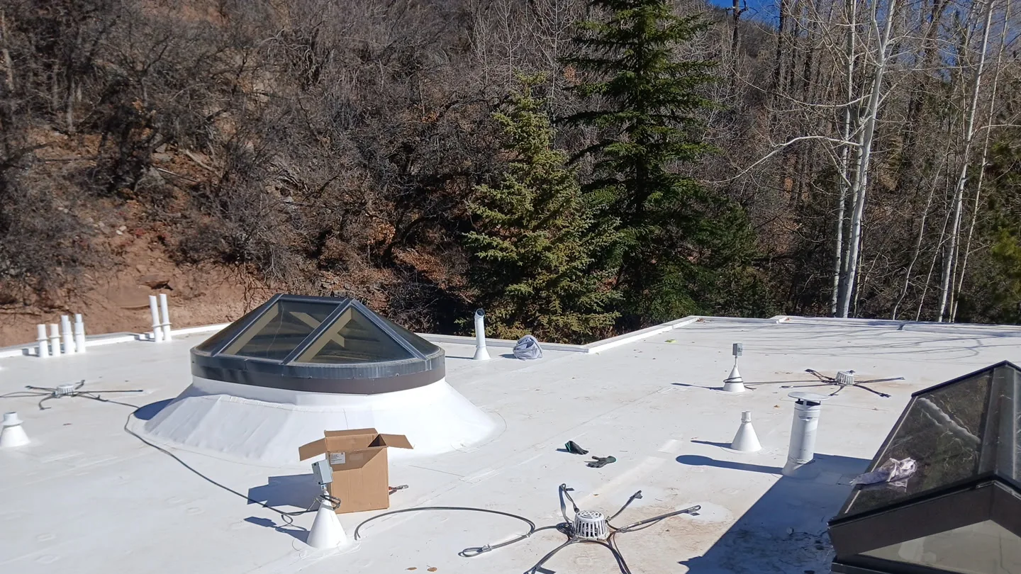 Finished white membrane roof with skylight curbs, drains, penetrations, and wooded mountain terrain