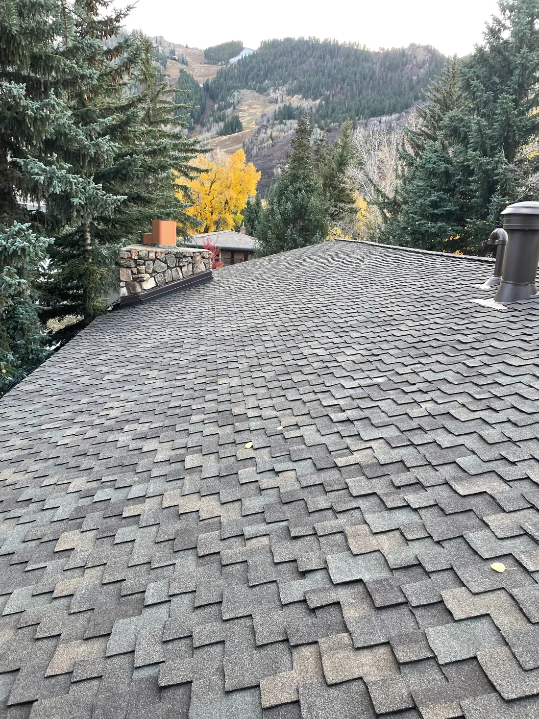 Presidential asphalt shingles installed around a stone chimney and roof penetrations with mountain terrain beyond